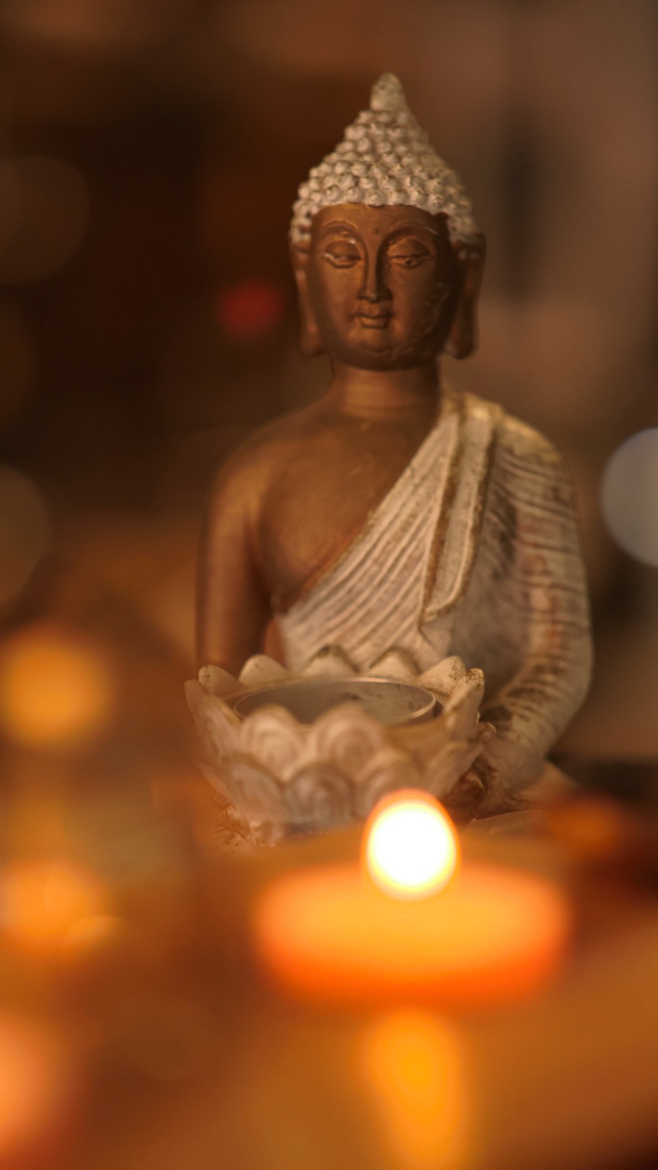 A seated Buddha statue in warm light with a softly blurred burning candle in the foreground