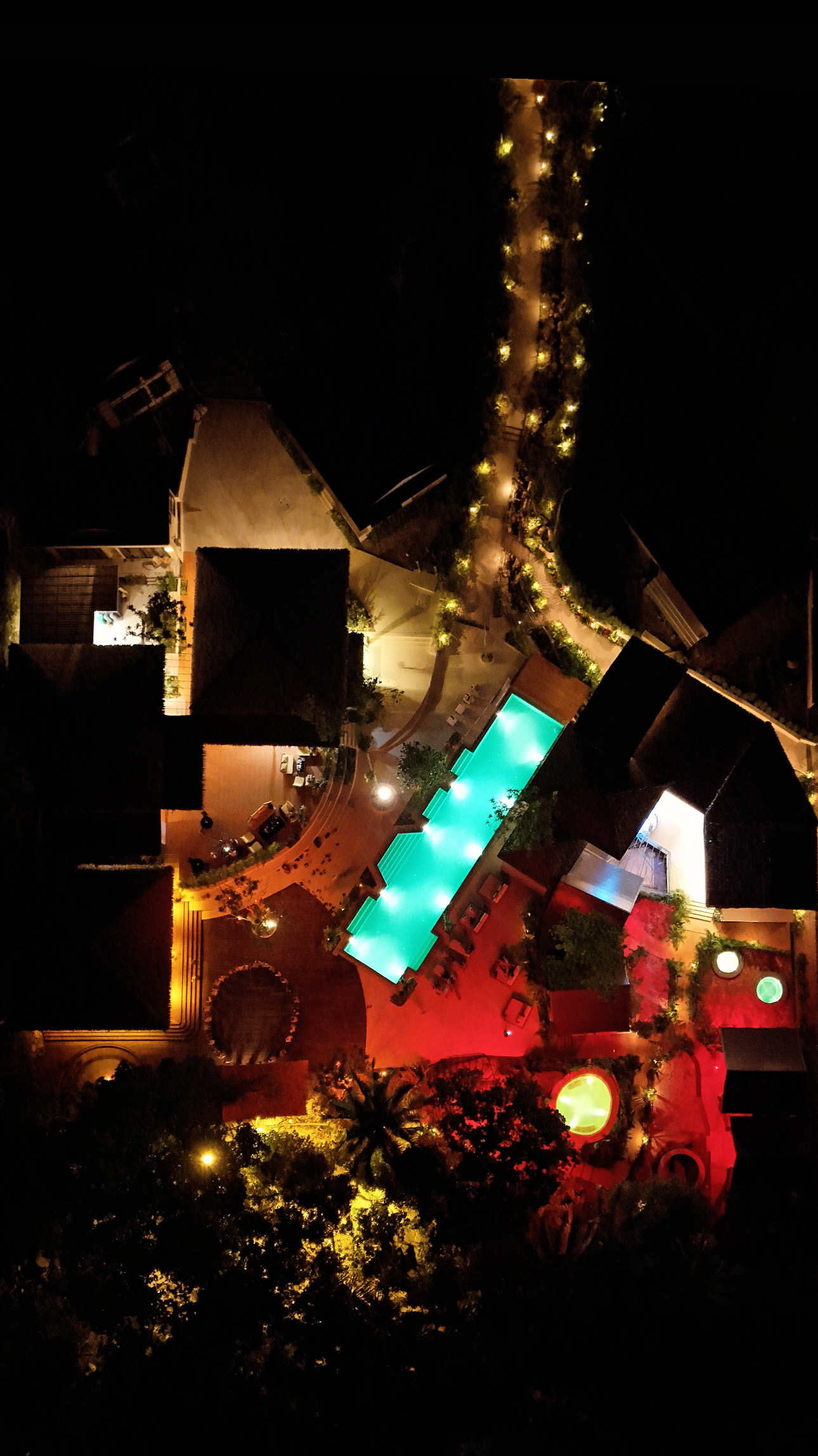 A pool and surrounding terraces glow in turquoise, red and warm lights against the dark night