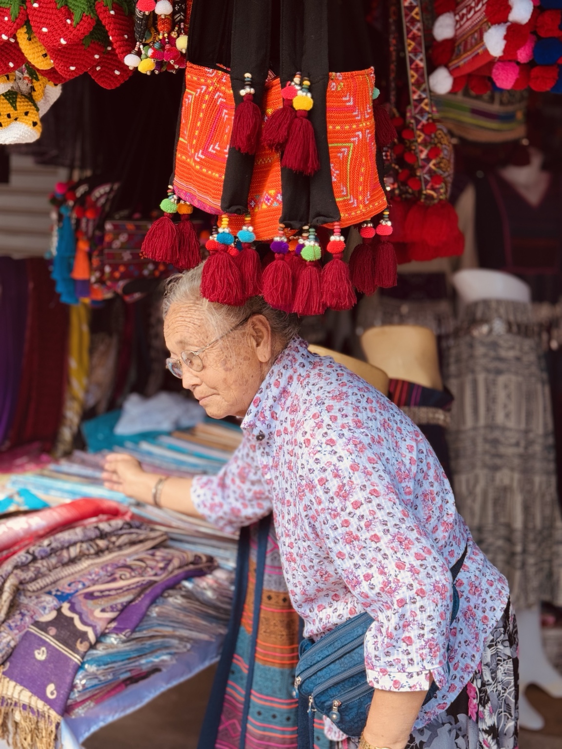 A person in a floral shirt looks up from folded fabrics beneath rows of colourful hanging decorations