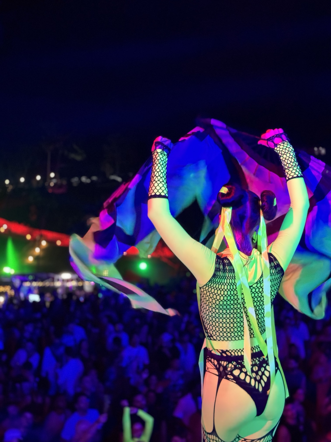 A performer raises colourful fabric above their head amid glowing neon colours and a night-time crowd