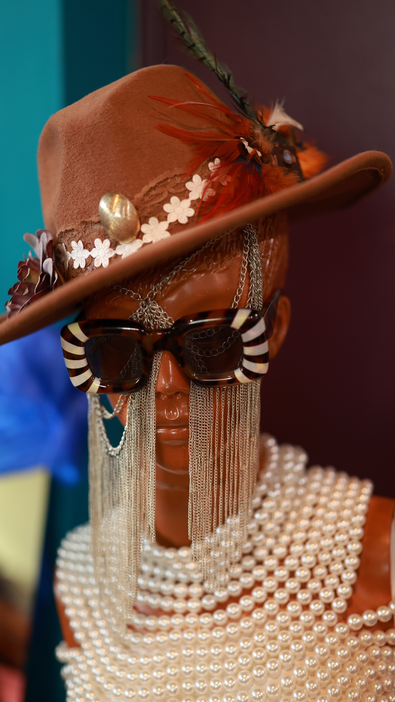 A hat, sunglasses and strands of pearls arranged on a display in warm light