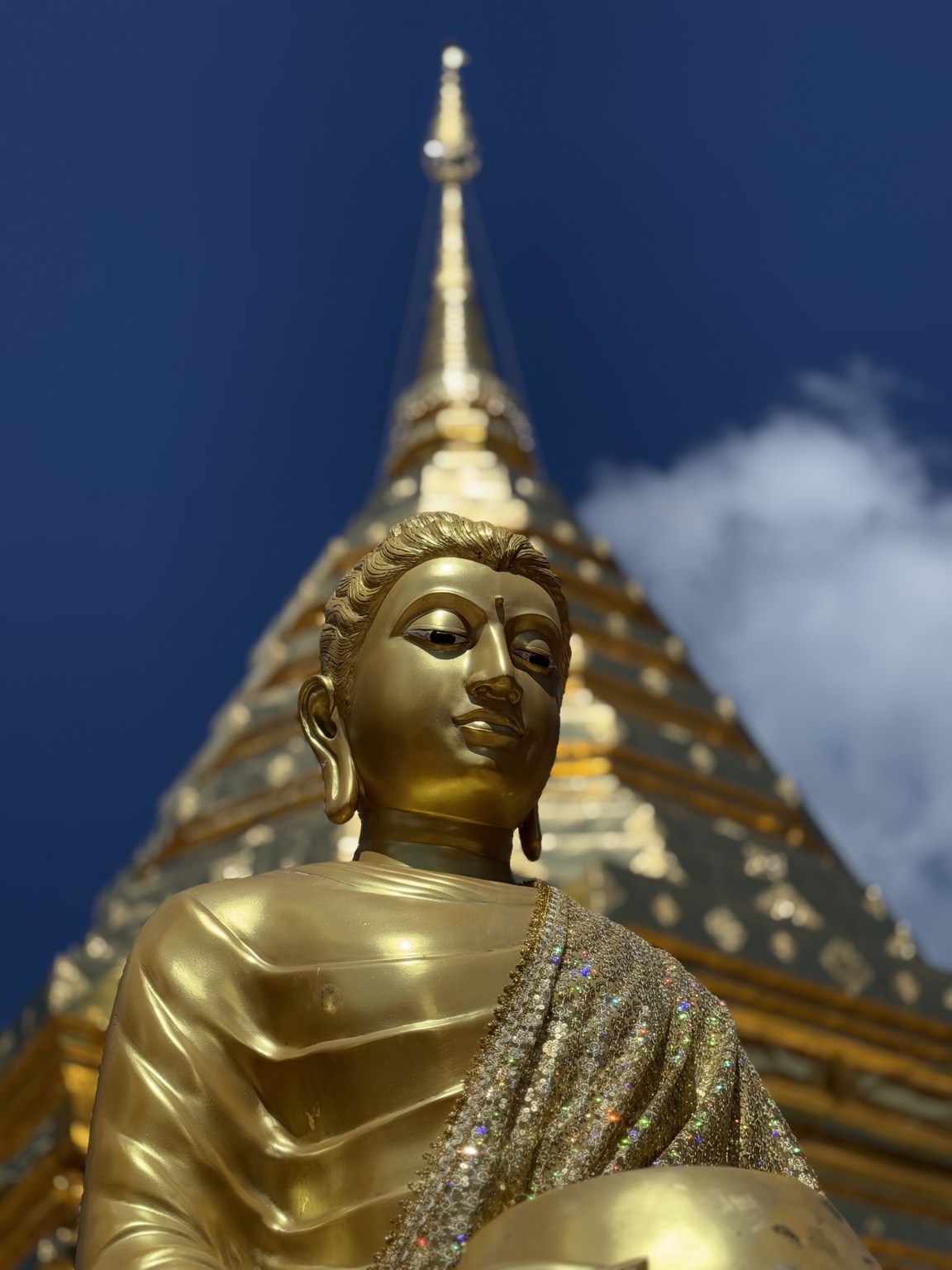 A golden seated Buddha statue rises in front of a gold temple spire and deep blue sky