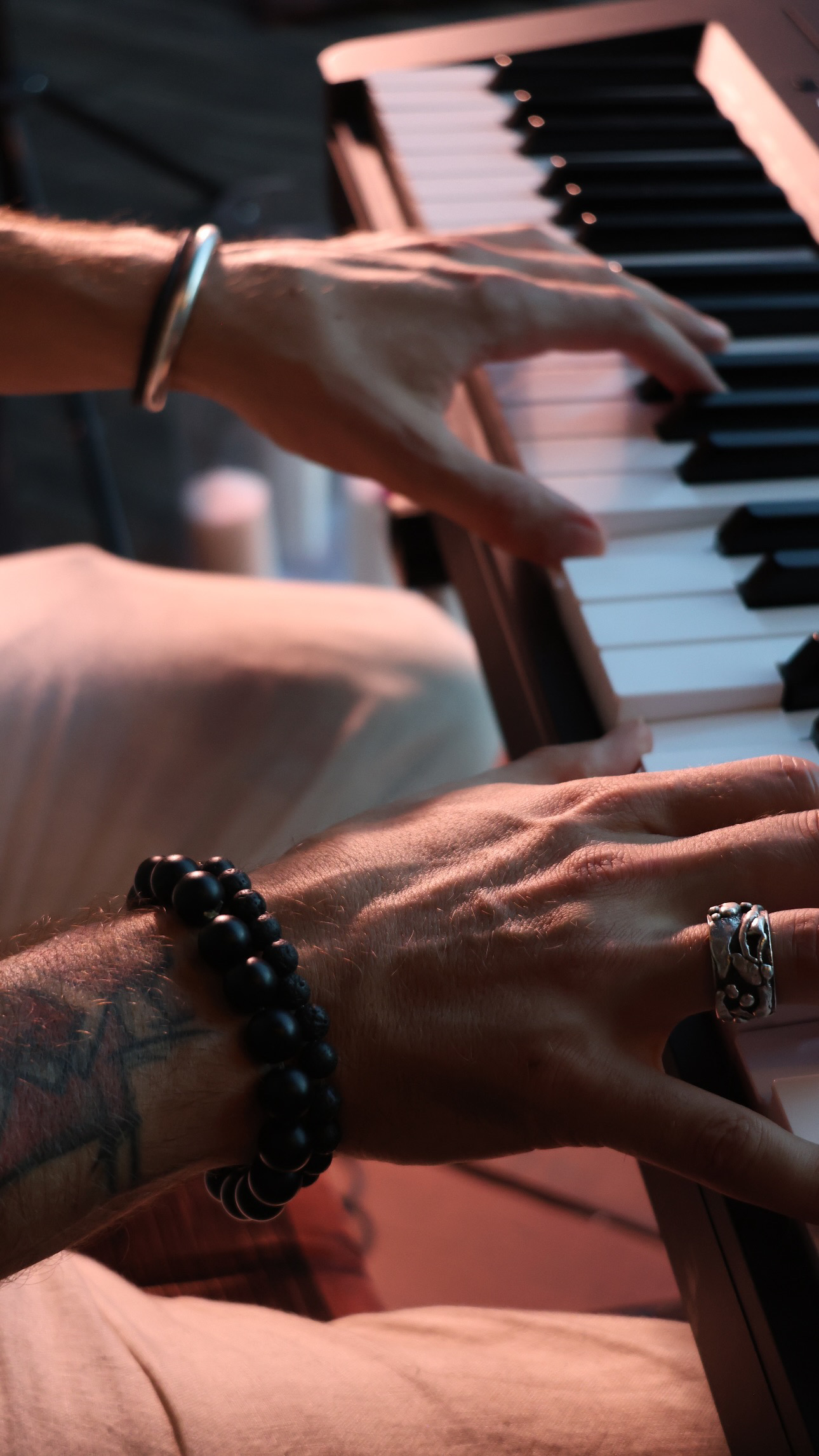 Several hands play a piano together in warm light, with dark and white keys filling the frame