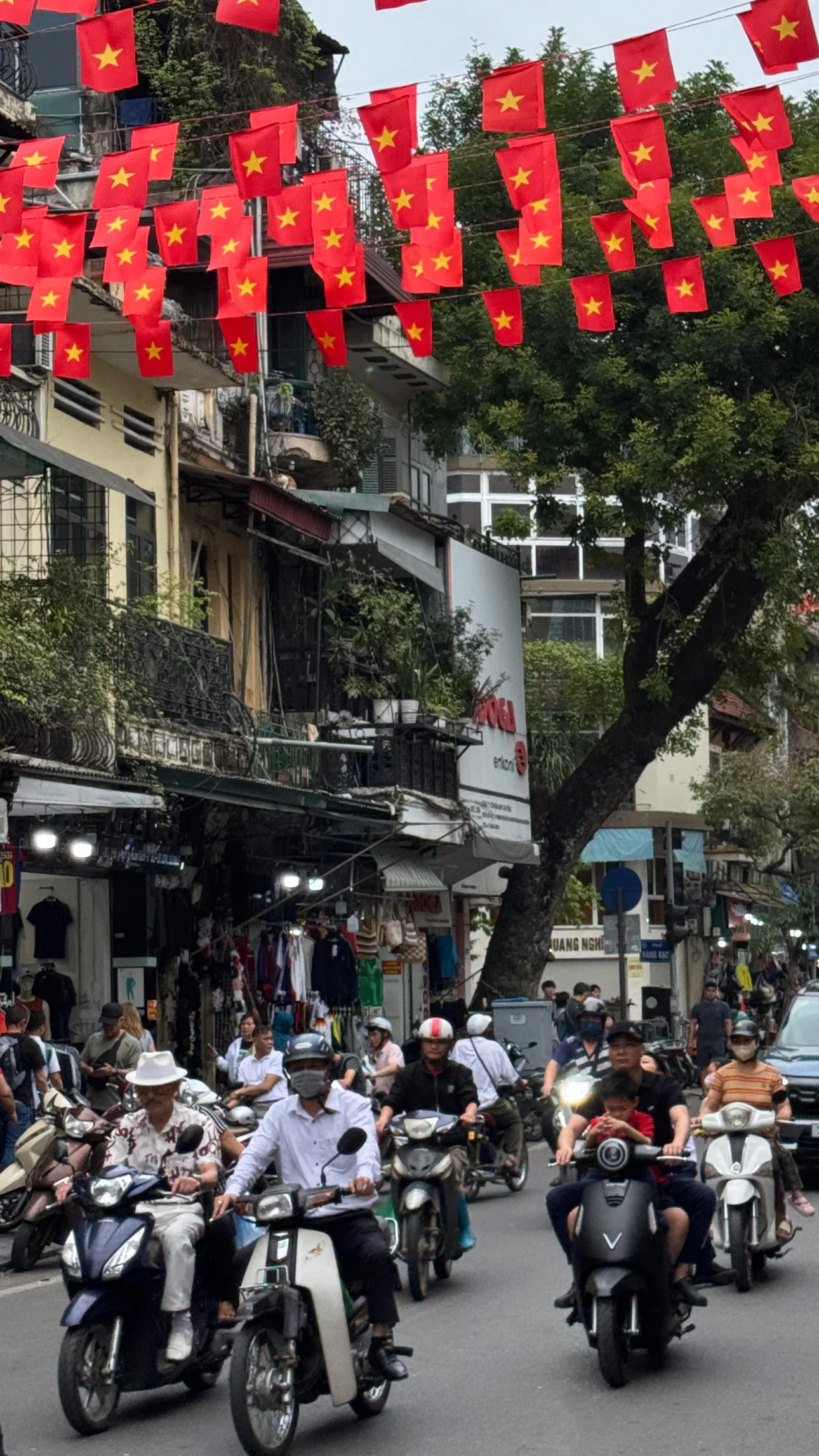 Motorbikes travel along a busy street beneath rows of red Vietnamese flags and balconies